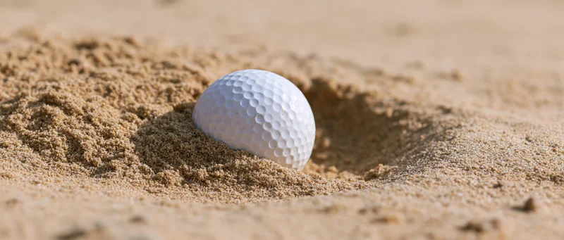 White golf ball partially embedded in a sand bunker depression on a golf course