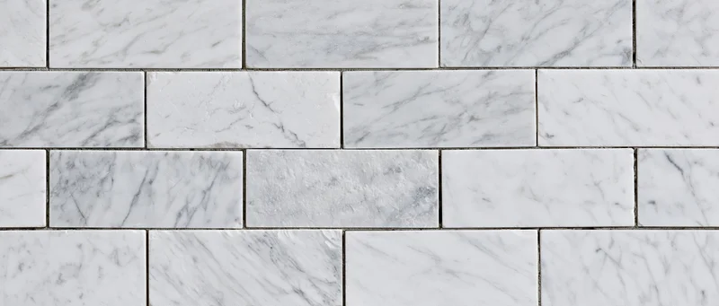 White marble tile wall surface arranged in staggered rows with gray veining and grout lines