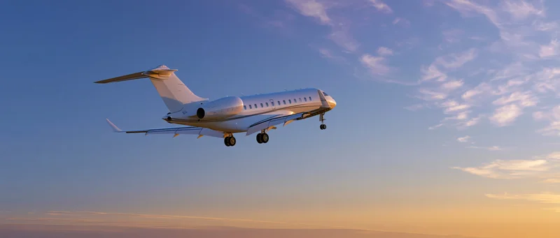 White private jet with landing gear down flying against sunset sky