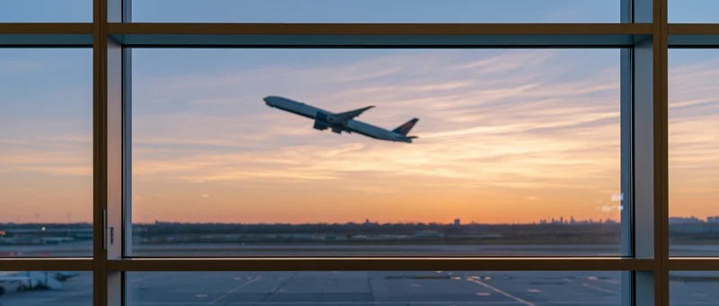 Airplane climbing steeply after takeoff viewed through airport terminal window