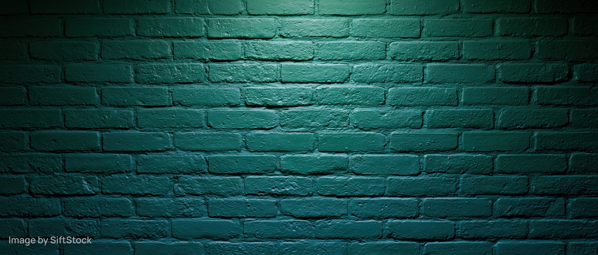 Painted brick wall illuminated by spotlight creating shadows and texture