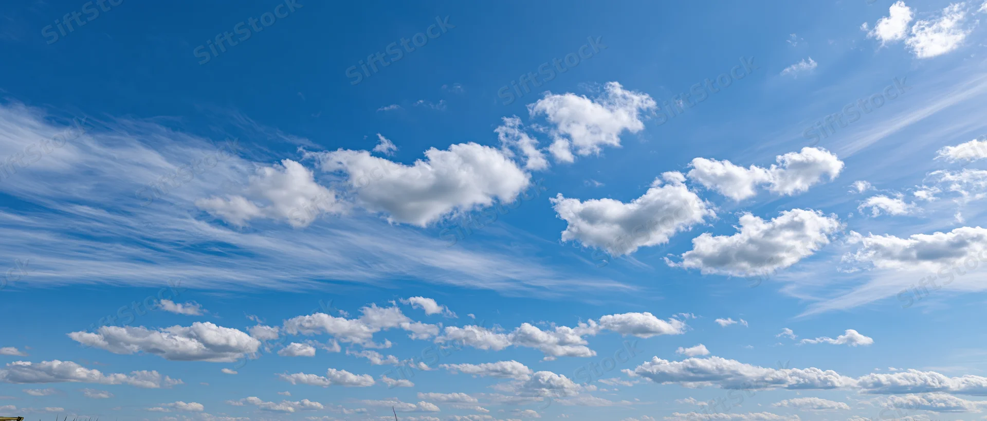 Wide panoramic view of a clear blue sky with scattered white clouds across the horizon