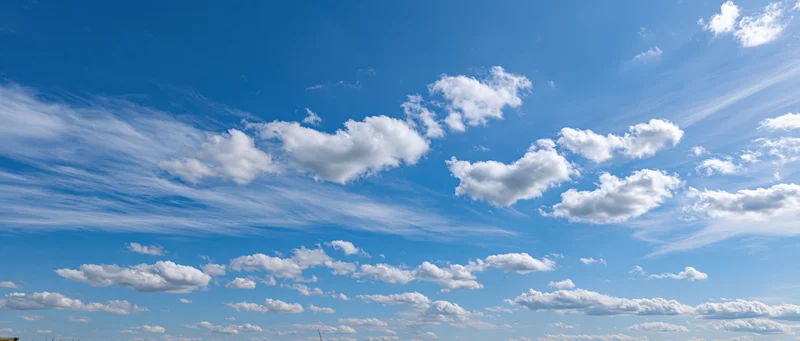 Wide panoramic view of a clear blue sky with scattered white clouds across the horizon