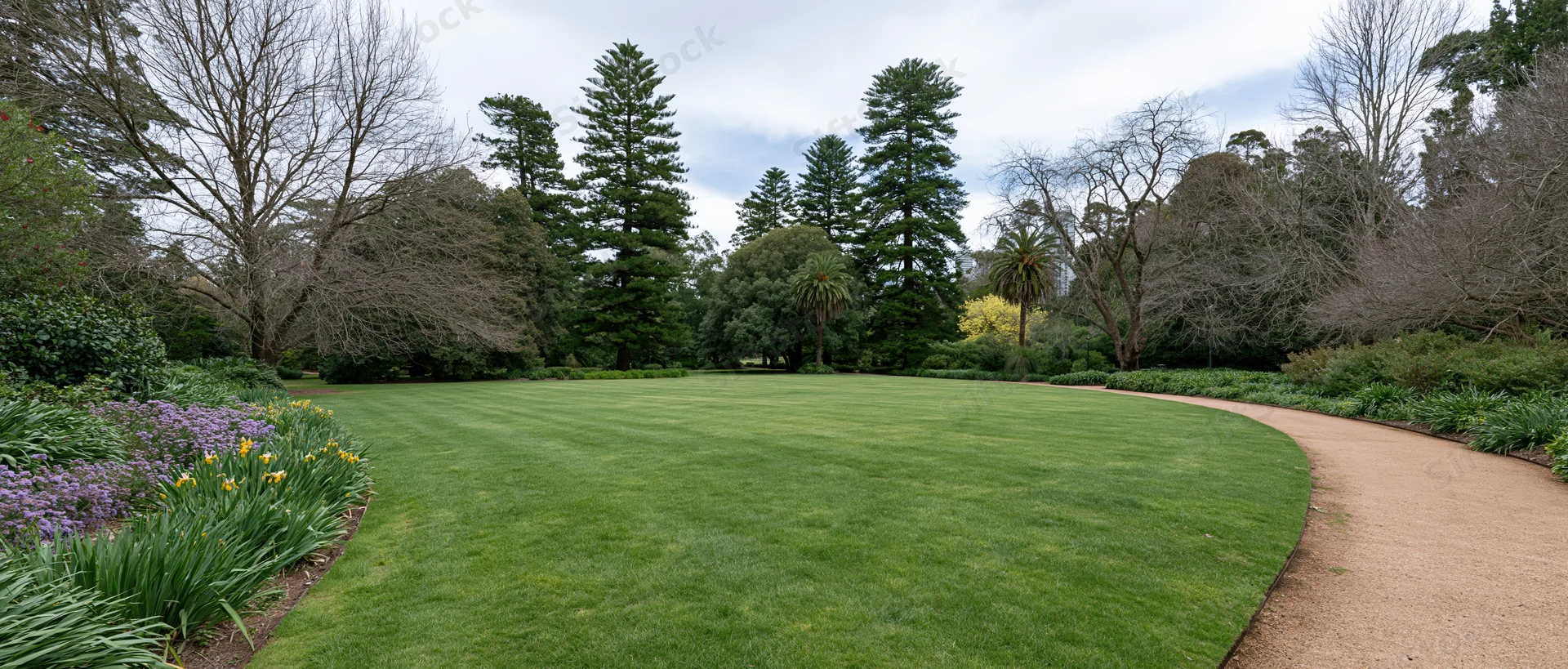 Wide view of a manicured park lawn with curved gravel path and surrounding trees and flower beds