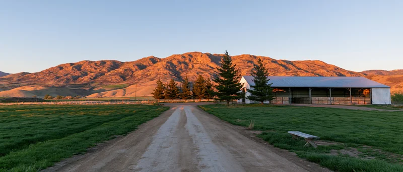 Dirt road leading to a barn on a farm at golden hour with mountains in the background
