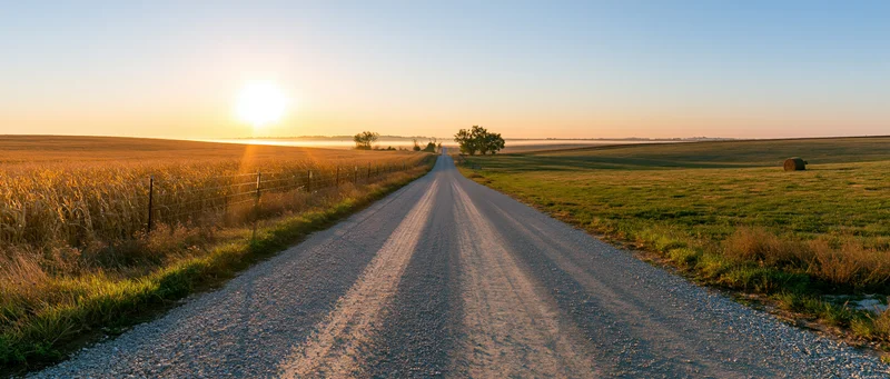 Gravel road stretching through rural fields at sunset