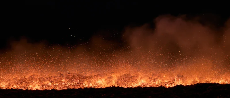 Intense fire burning low across dark landscape at night
