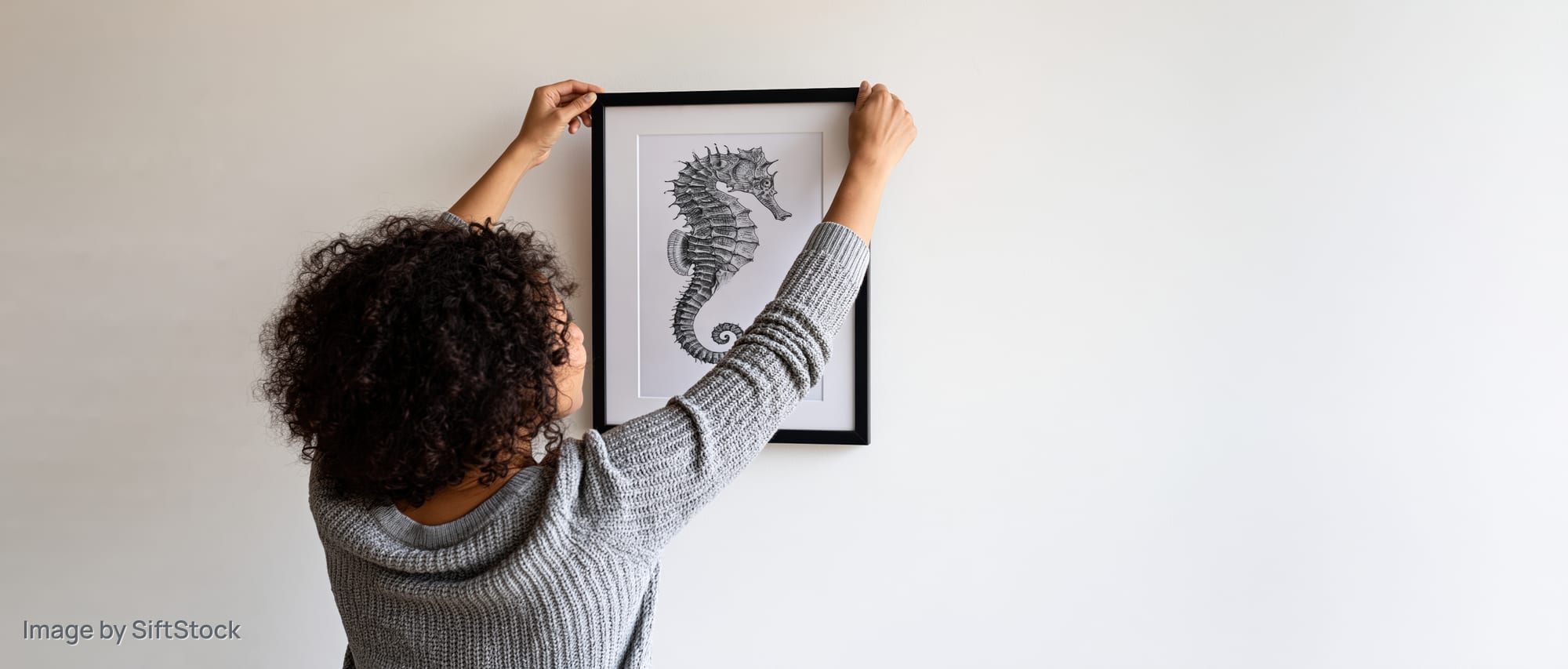 Woman hanging a framed seahorse artwork on a white wall