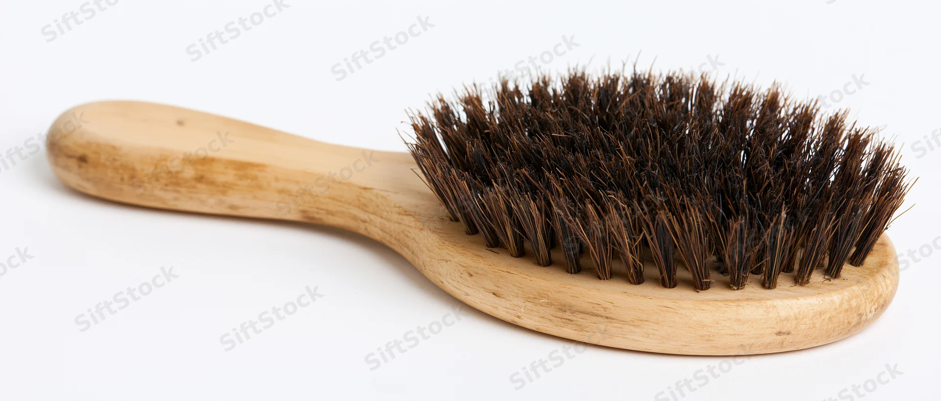 Worn wooden hairbrush with dark boar bristles lying flat on white background