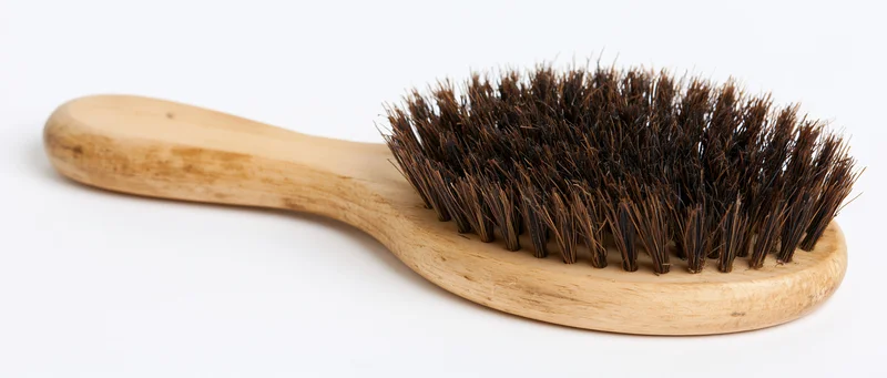 Worn wooden hairbrush with dark boar bristles lying flat on white background