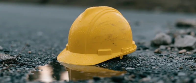 Yellow hard hat resting on wet asphalt pavement with puddle reflection