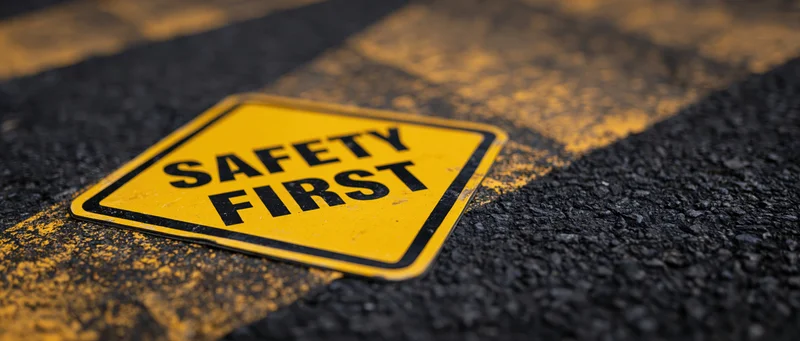 Yellow diamond-shaped safety sign reading safety first on asphalt pavement with yellow stripes