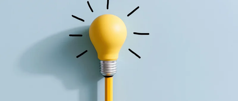 Yellow lightbulb resting on top of a yellow pencil against a blue background