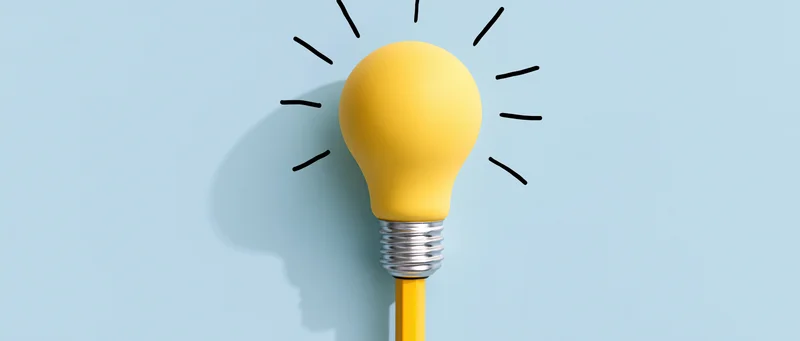 Yellow lightbulb resting on top of a yellow pencil against a light blue background