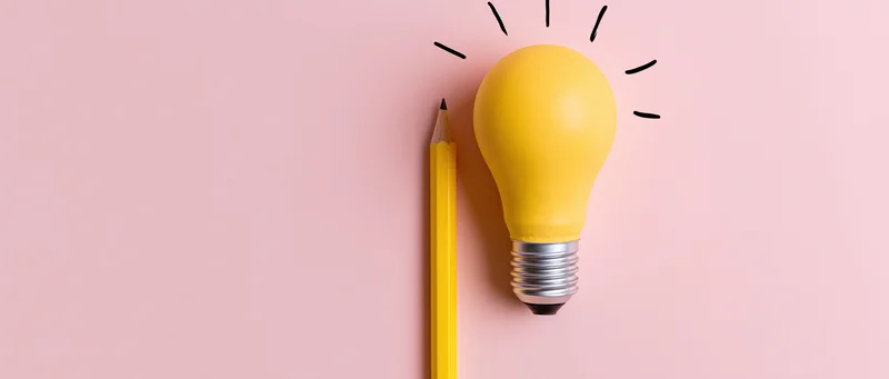 Yellow lightbulb and pencil arranged upright on pink surface symbolizing idea generation