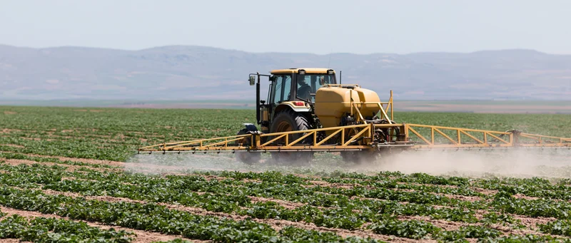 Yellow tractor with boom sprayer moving across a large crop field
