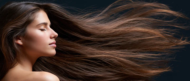 Woman in profile with long flowing chestnut hair, eyes closed, against dark background