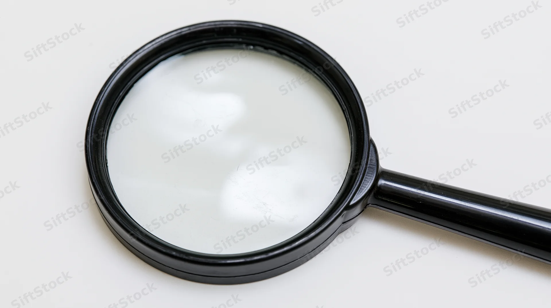 Black plastic handheld magnifying glass lying flat on white surface