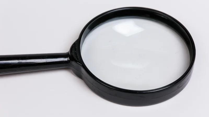 Black plastic handheld magnifying glass lying flat on white surface