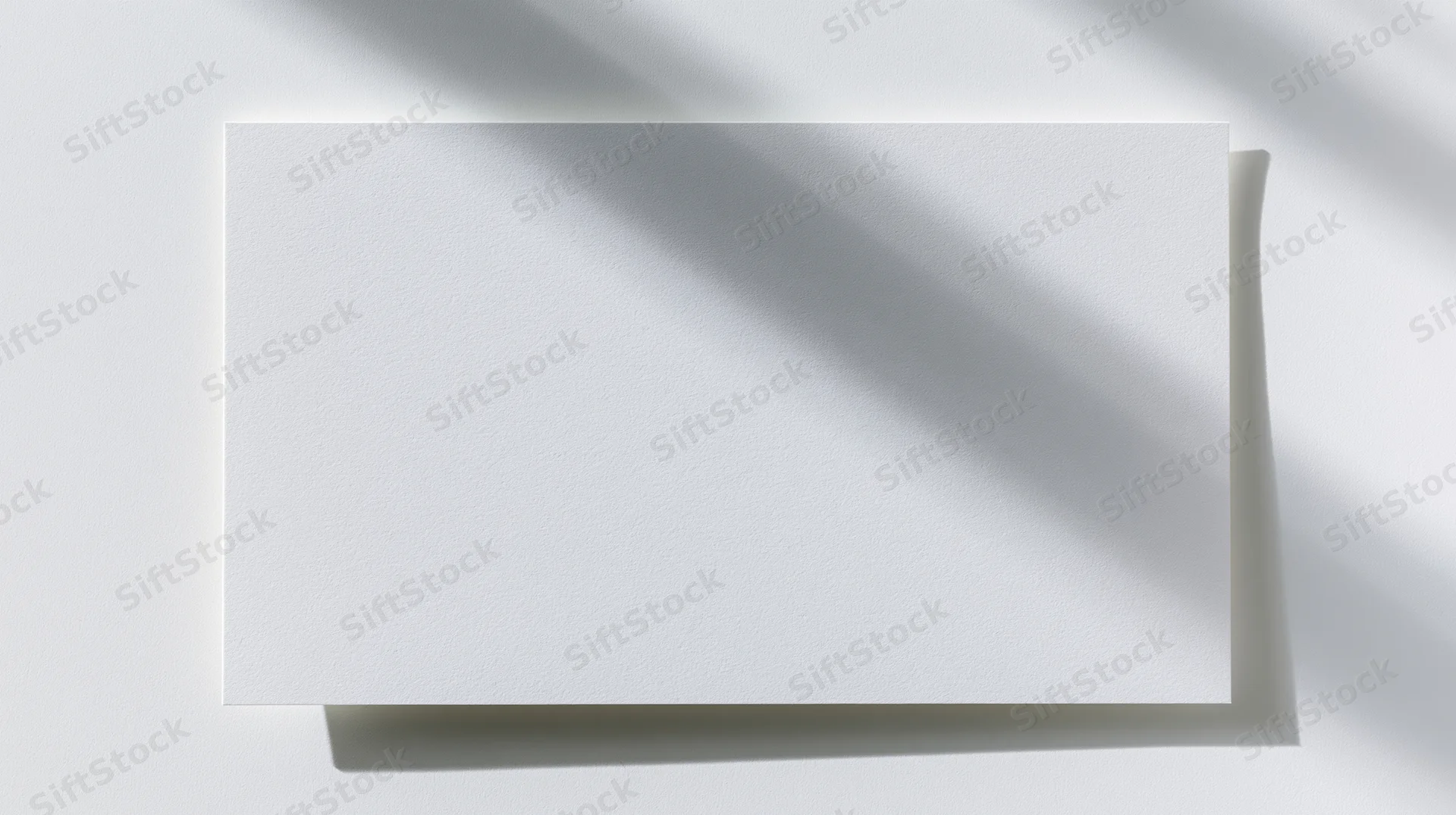 Blank white card lying flat on a white surface with shadows from overhead light