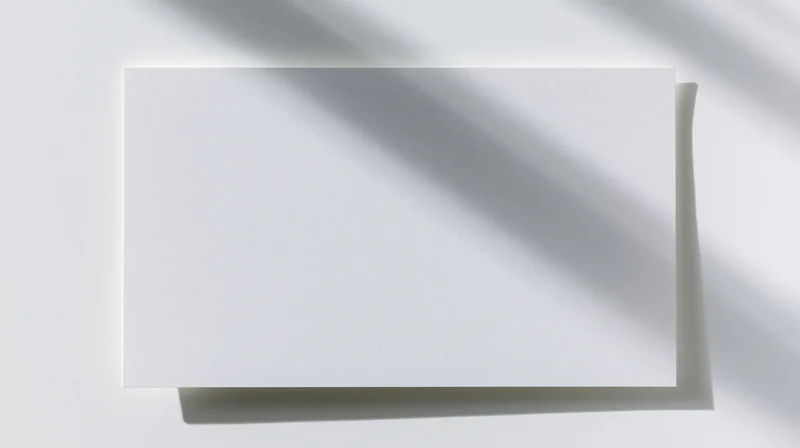 Blank white card lying flat on a white surface with shadows from overhead light
