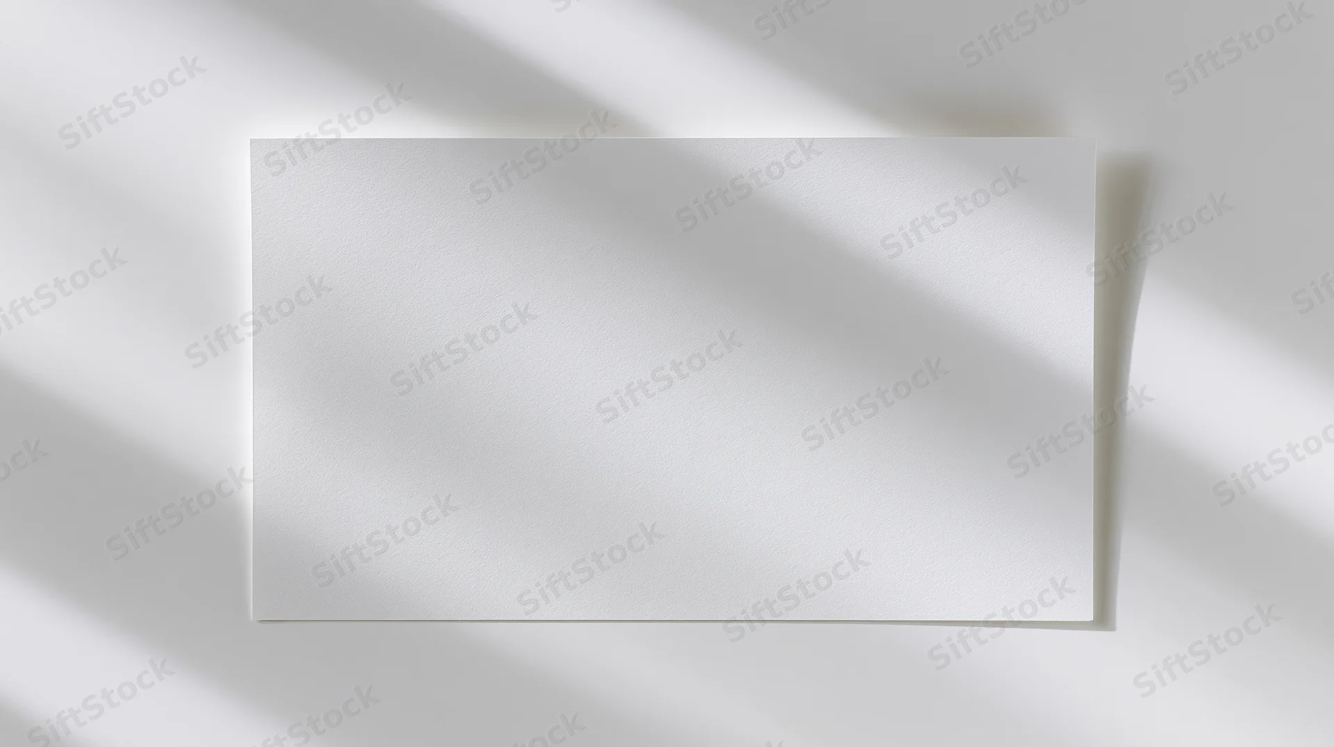 Blank white card lying flat on a white surface with soft shadows and copyspace