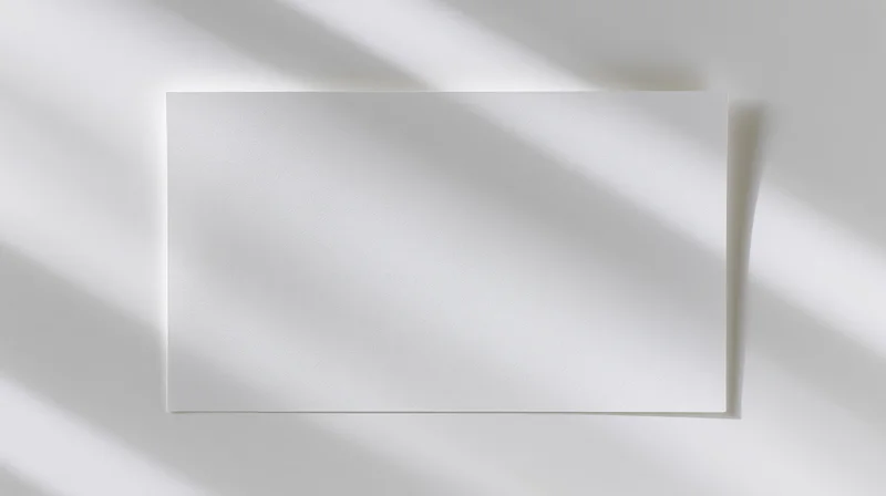 Blank white card lying flat on a white surface with soft shadows and copyspace