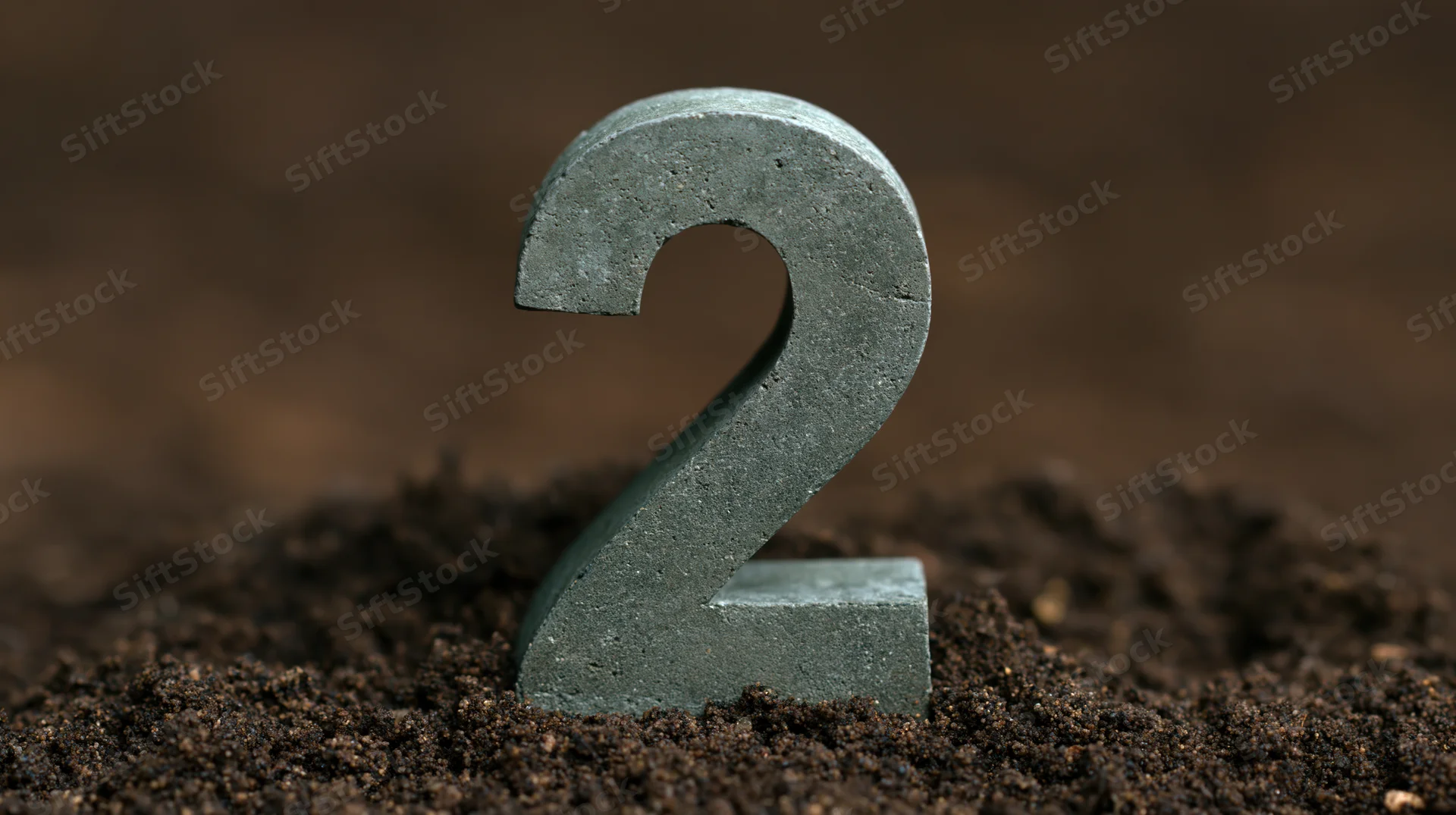 Concrete number two standing upright in soil with blurred background