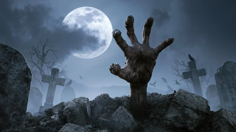 Decayed hand clawing from broken grave under full moon in foggy cemetery