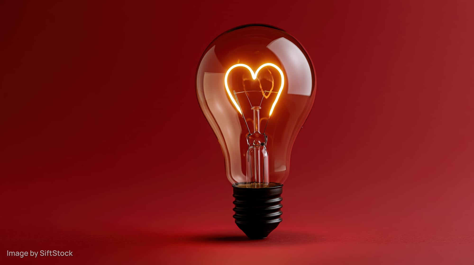 Glowing heart-shaped filament inside a glass lightbulb on red background