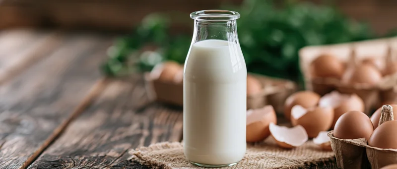 Glass bottle of fresh milk on wooden table surrounded by eggs and eggshells