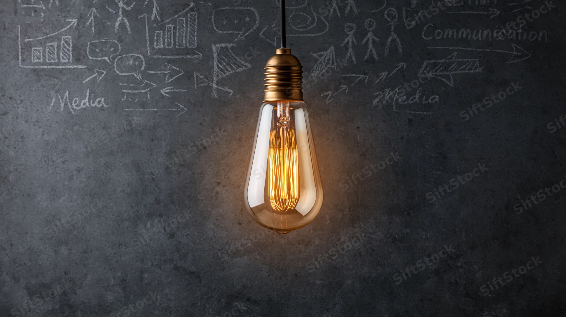 Glowing edison-style lightbulb hanging in front of a chalkboard with sketches of communication and media concepts