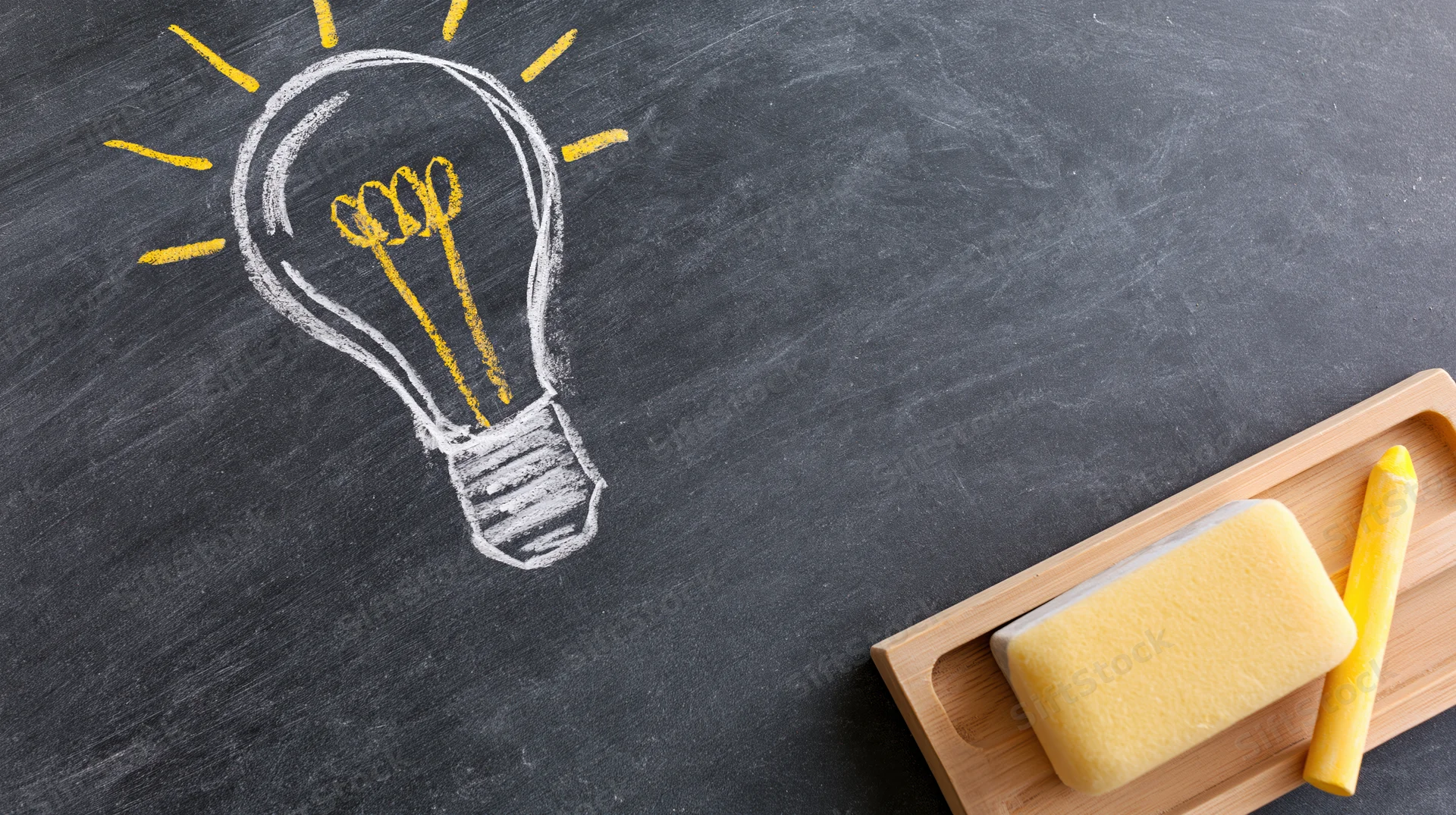 Chalk-drawn lightbulb on blackboard with sponge and yellow chalk on wooden tray