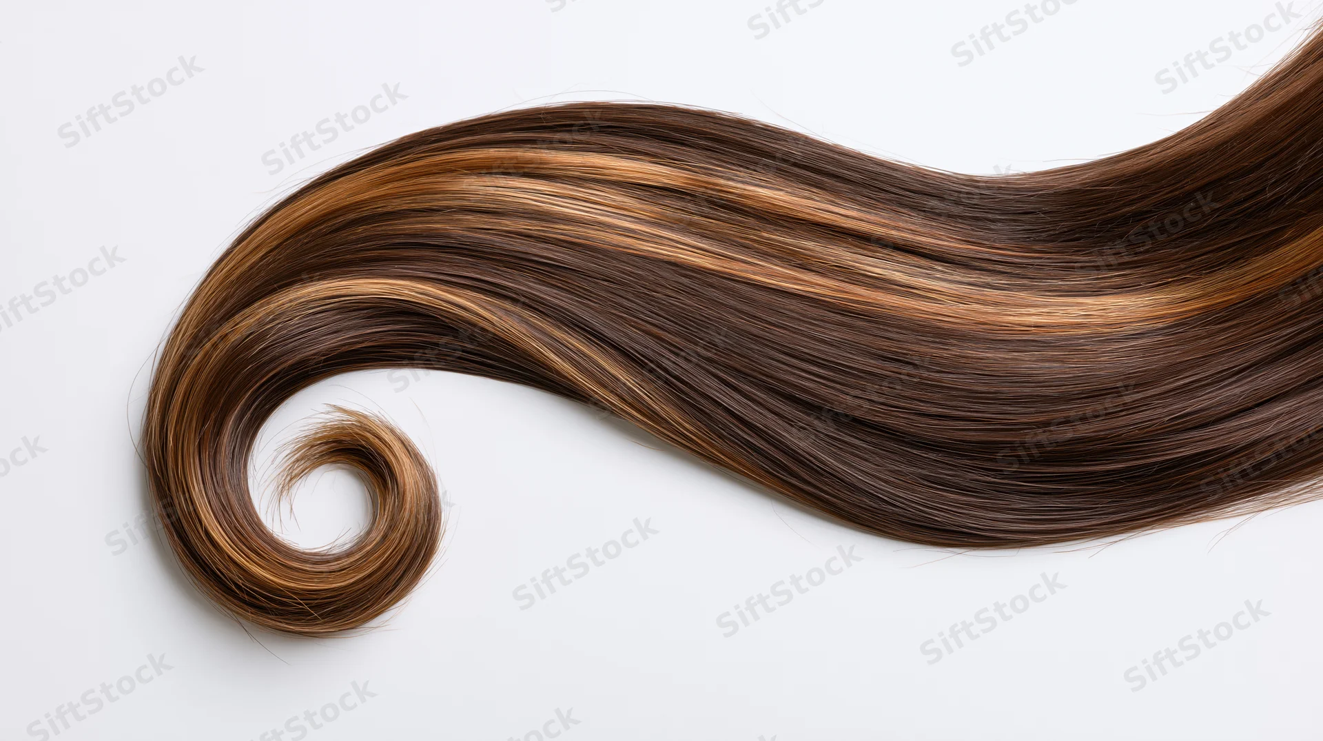 A loose curl of long brown hair with caramel highlights arranged on a white surface