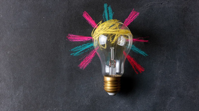 Incandescent light bulb with colorful chalk rays on dark chalkboard surface