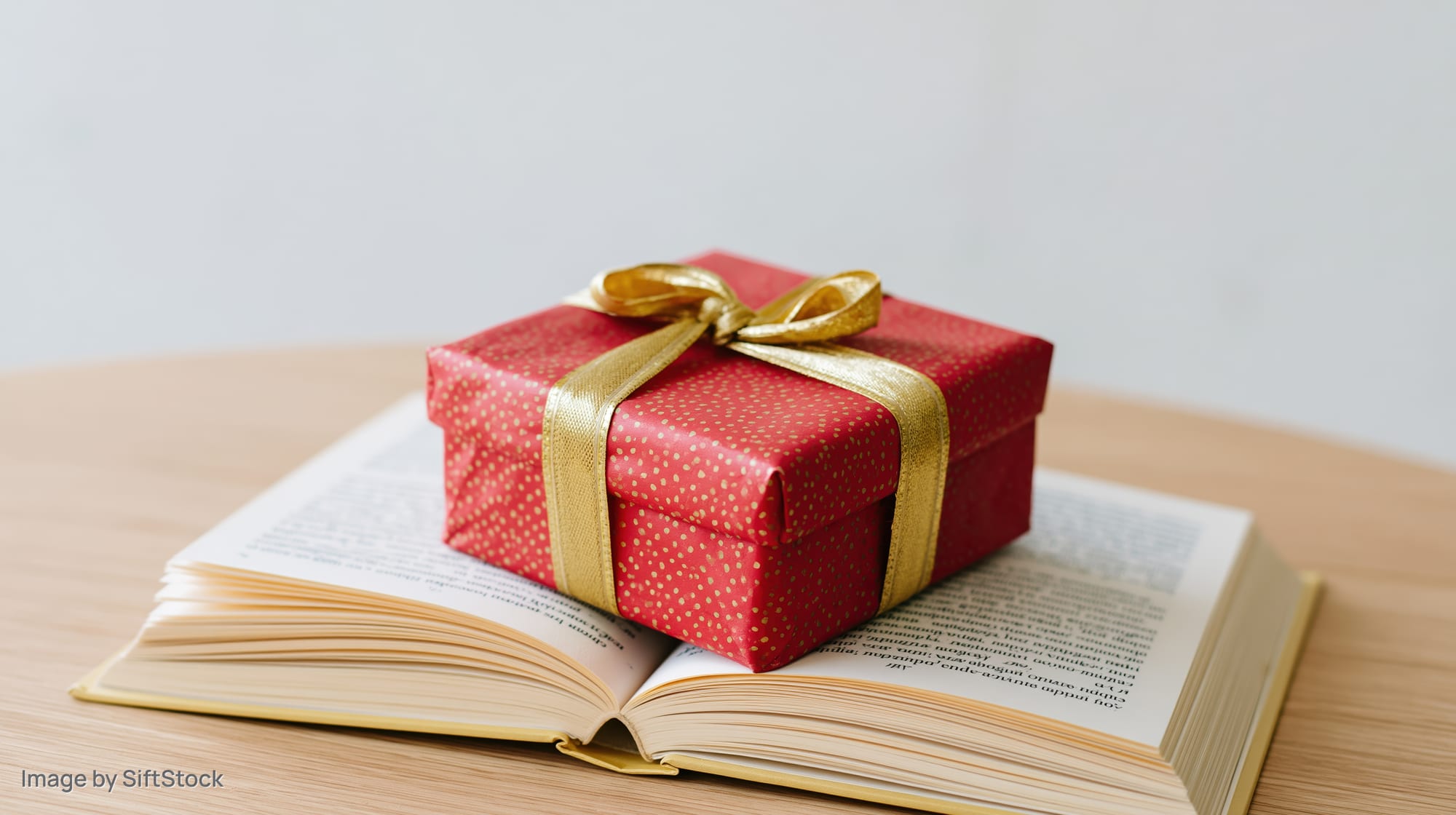 Red gift box with gold ribbon resting on open book on wooden table