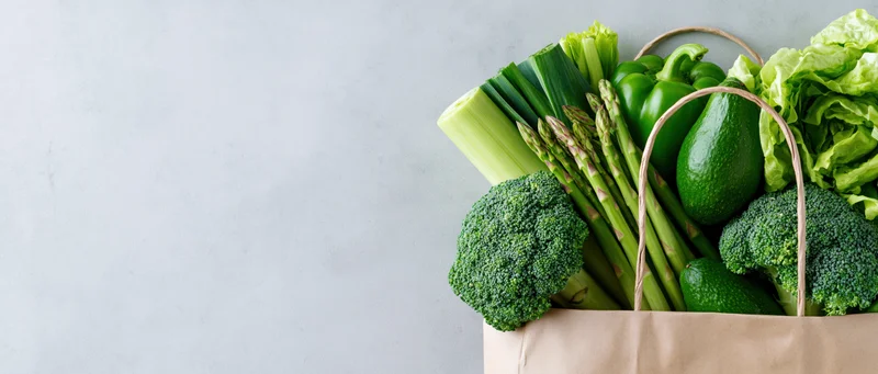 Reusable paper bag filled with green vegetables on a light gray countertop