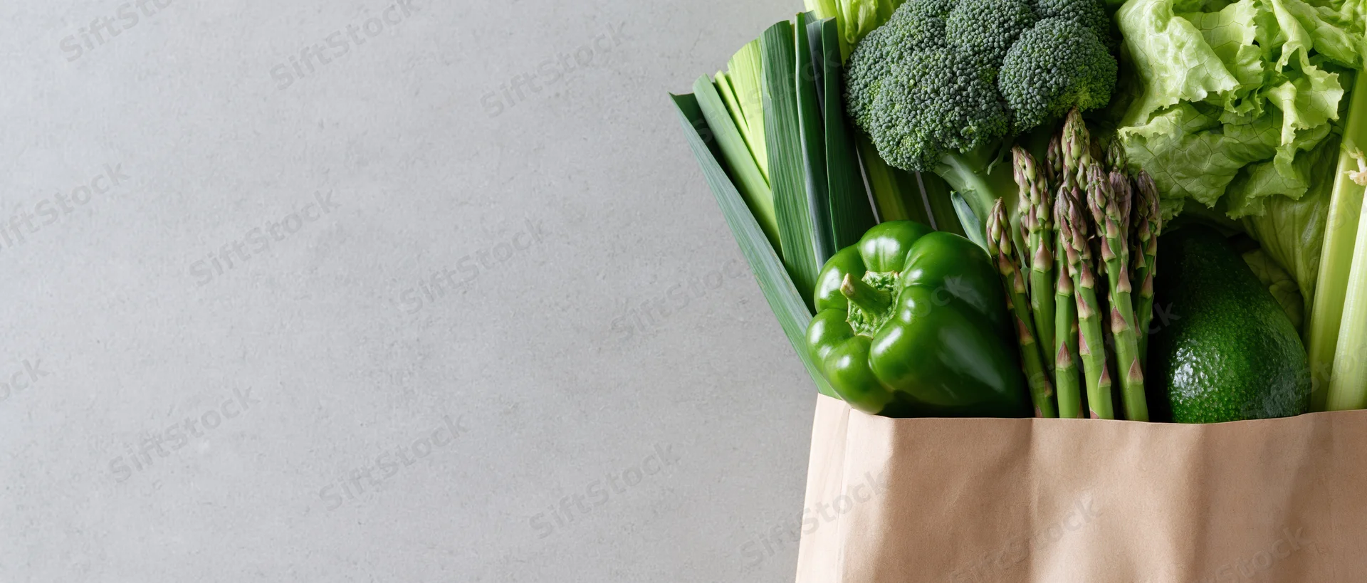 Reusable paper bag filled with fresh green vegetables on a gray surface