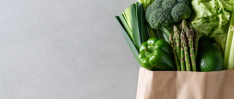 Reusable paper bag filled with fresh green vegetables on a gray surface