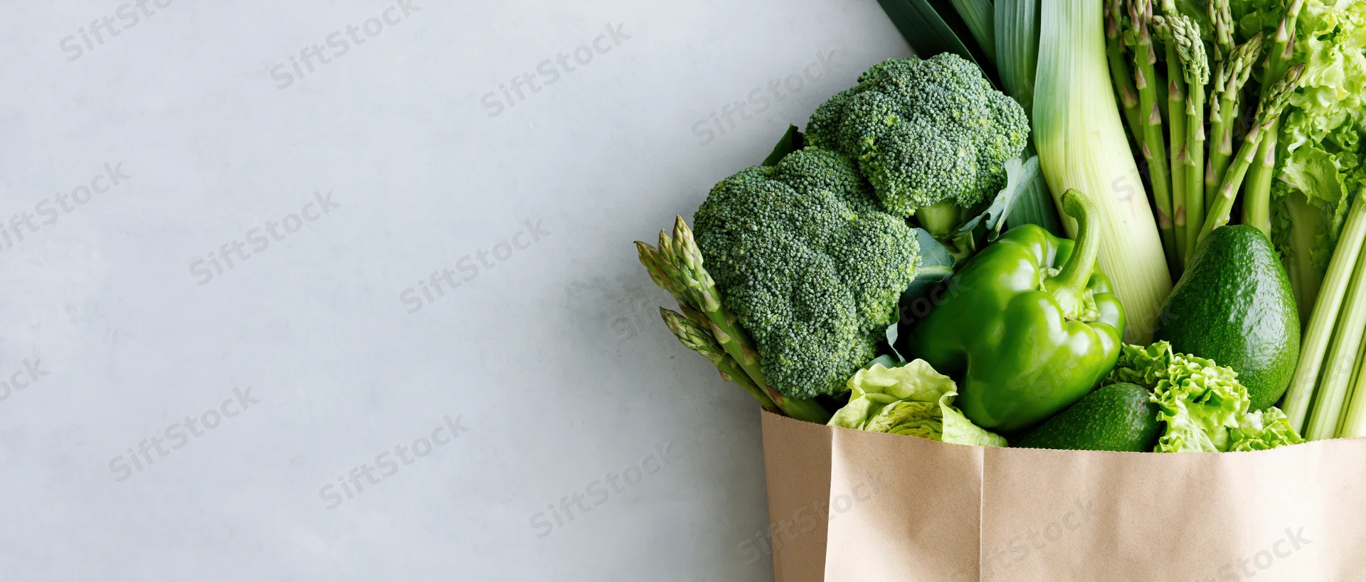 Reusable paper bag filled with fresh green vegetables on light surface