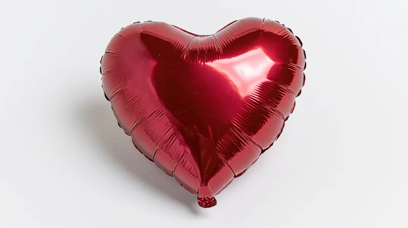 Shiny red metallic foil heart-shaped balloon floating against white background