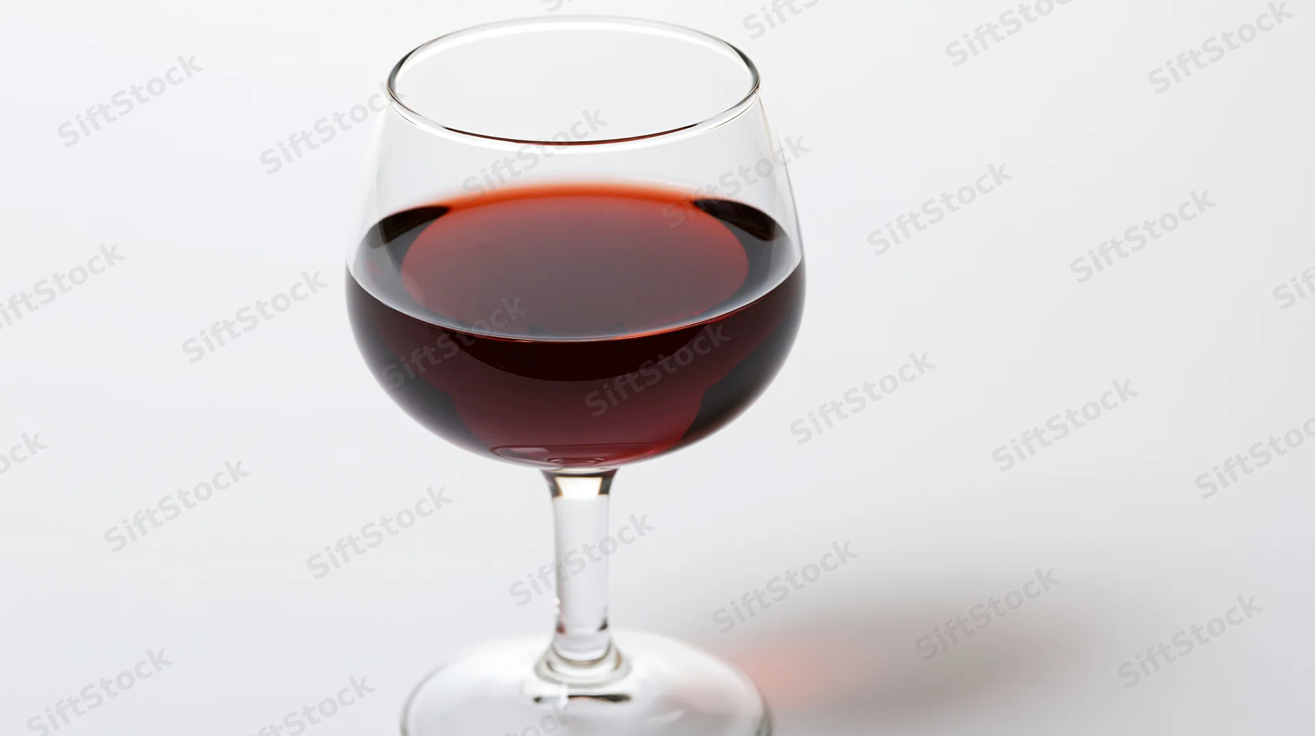 A burgundy-style wine glass half-filled with deep red wine on a white background