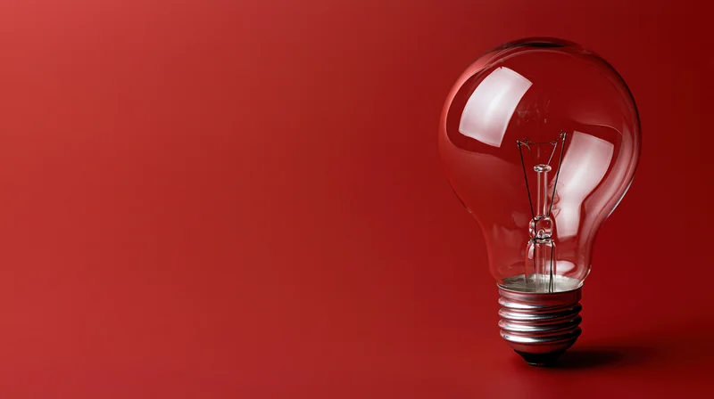 Clear glass incandescent light bulb with visible filament on red background