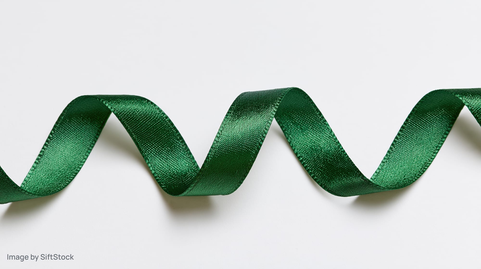 Dark green satin ribbon curling in a zigzag pattern on white background