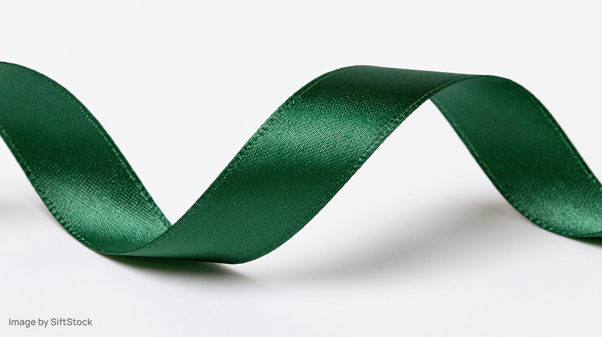 Dark green satin ribbon curling in a loose zigzag pattern on white background