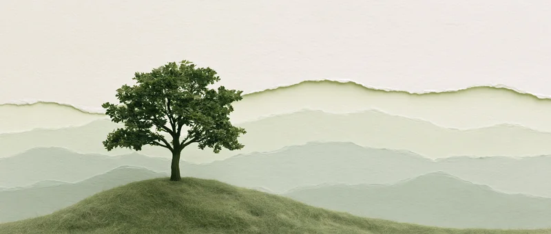 A single tree stands on a grassy hill with layered misty mountains in the background