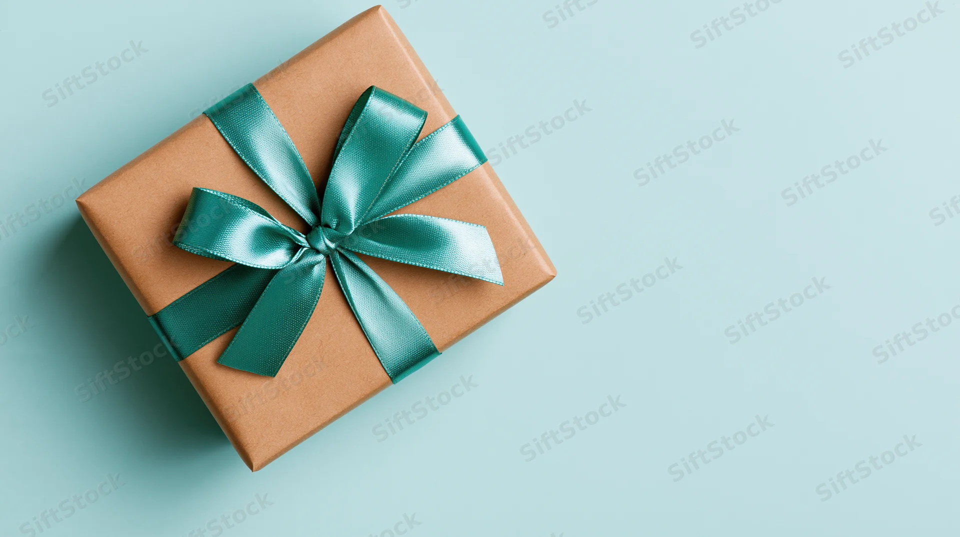 Gift box wrapped in brown kraft paper with teal ribbon bow on light blue surface