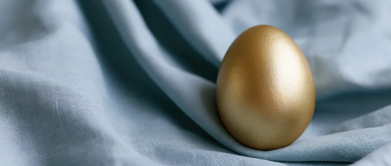Golden egg resting upright on draped blue fabric