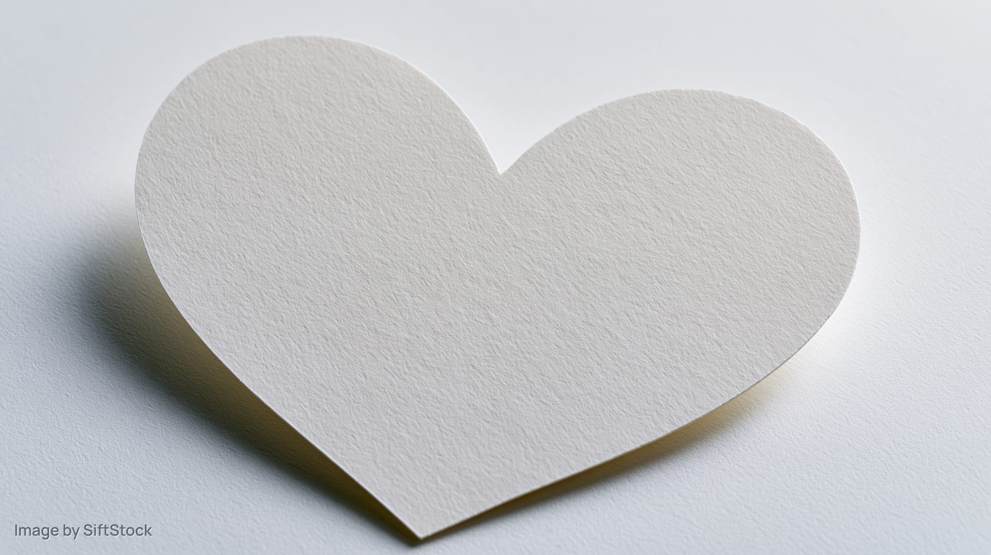 A pale white heart cutout made of matte cardstock lying flat on a white surface