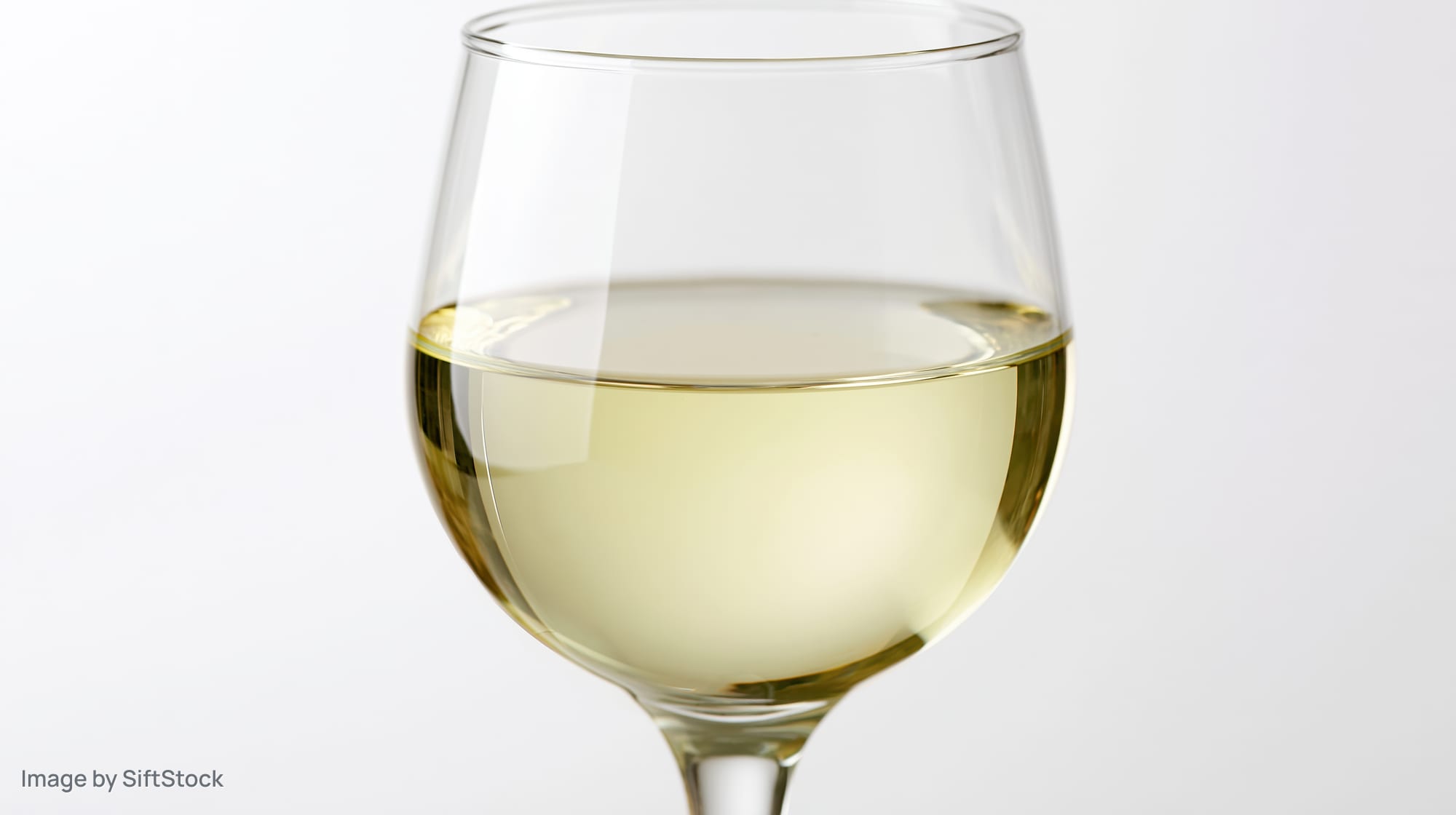 A tulip-shaped wine glass half-filled with pale straw-colored white wine on a white background